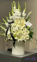<h2>باکس گل ترحیم لاکچری سفید</h2> <p>این آرایش گل سفارشی، با الهام از زیبایی و وقار گل‌های سفید، انتخابی ایده‌آل برای ابراز همدردی و احترام در مراسم ترحیم است. ترکیب گل‌های شمشیری بلند، لیلیوم معطر، آنتریم و داوودی در کنار روبان مشکی ساتن، ظاهری لوکس و در عین حال متین به این باکس بخشیده است.</p> <ul> <li><strong>ترکیب گل‌ها:</strong> گل شمشیری سفید، لیلیوم، آنتریم و داوودی</li> <li><strong>طراحی:</strong> گلدان سفارشی سفید با خطوط عمودی و روبان مشکی</li> <li><strong>مناسب برای:</strong> پیام تسلیت، مراسم ختم و ترحیم</li> <li><strong>ویژگی‌ها:</strong> گل‌های تازه و طبیعی، طراحی مدرن و شیک</li> </ul> <p>این باکس گل، پیام تسلیت شما را با شکوه و وقار به بازماندگان منتقل می‌کند.</p>